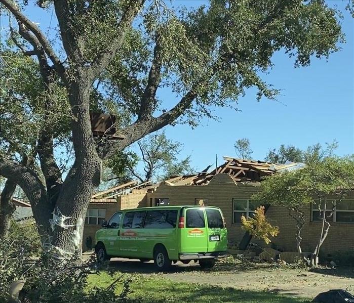 SERVPRO van parked in a driveway of a home in Dallas, TX that is missing their roof from storm damage. 