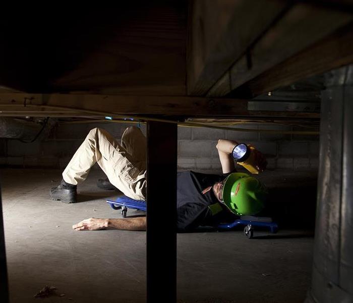 SERVPRO employee in a hard hat inspecting a crawl space with a flashlight