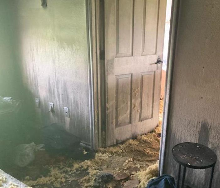 Photo of an open door, surrounding walls, and household items covered with smoke and soot.