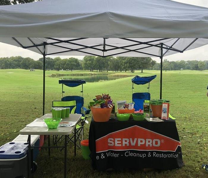The Servpro table is set up on a golf course under a white tent with games and raffle items. 